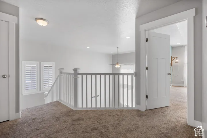 Neutral-toned interior space featuring white balustrade railings, interior doors with shaker-style panels, window shutters, recessed lighting, and a ceiling fan