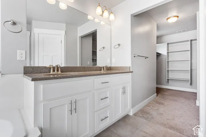 Double vanity featuring white cabinetry, stone-composite countertops, dual under-mount sinks, and a large wall-mounted mirror