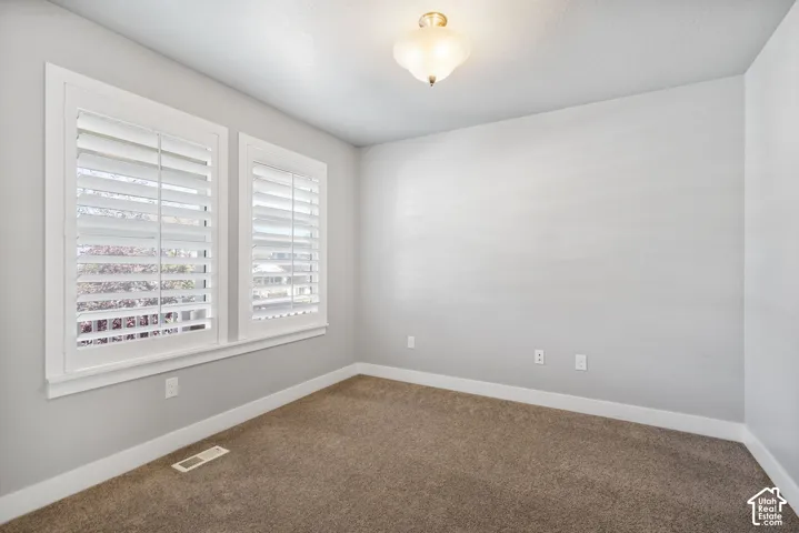 Neutral-toned interior space featuring wall-to-wall carpeting, dual windows with white plantation shutters, and a central flush-mount ceiling light fixture
