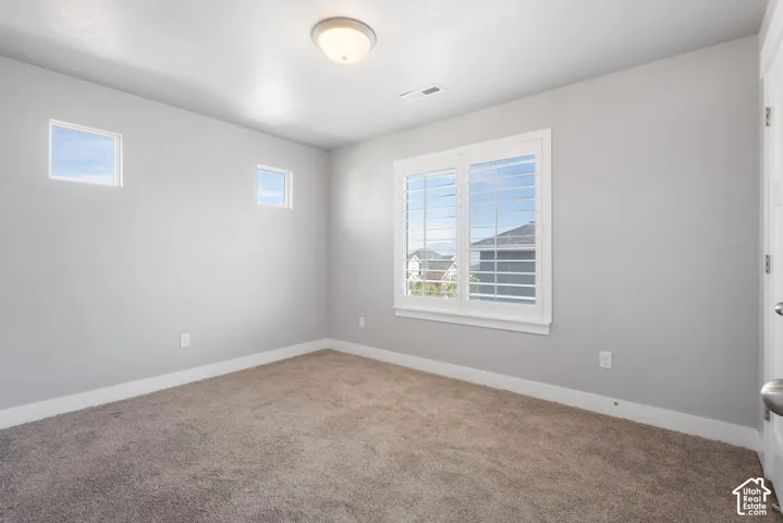 Neutral-toned interior room featuring wall-to-wall carpeting, white plantation shutters, dual small square windows, and a central dome-style ceiling light fixture