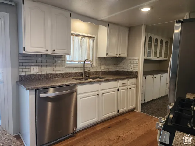Kitchen featuring white cabinetry, subway tile backsplash, stone-finish countertops, stainless steel dishwasher, and wood-finish flooring