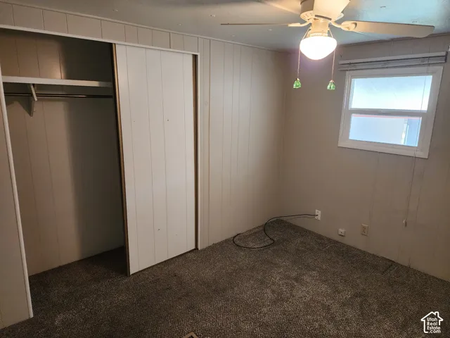 Interior space featuring wall-paneling, carpet flooring, a sliding-door closet with built-in shelving, and a ceiling fan with integrated lighting