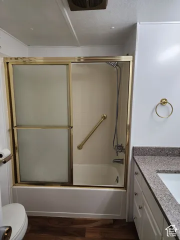 Shower and tub combination featuring sliding glass doors with gold-tone framing, wall-mounted hand shower, and a built-in grab bar, paired with a vanity featuring a solid surface countertop and white cabinetry