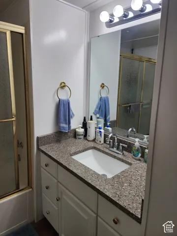 Bathroom vanity featuring a solid surface countertop with an integrated basin, white cabinetry with brass-finish hardware, a full-length wall mirror, and a multi-light fixture
