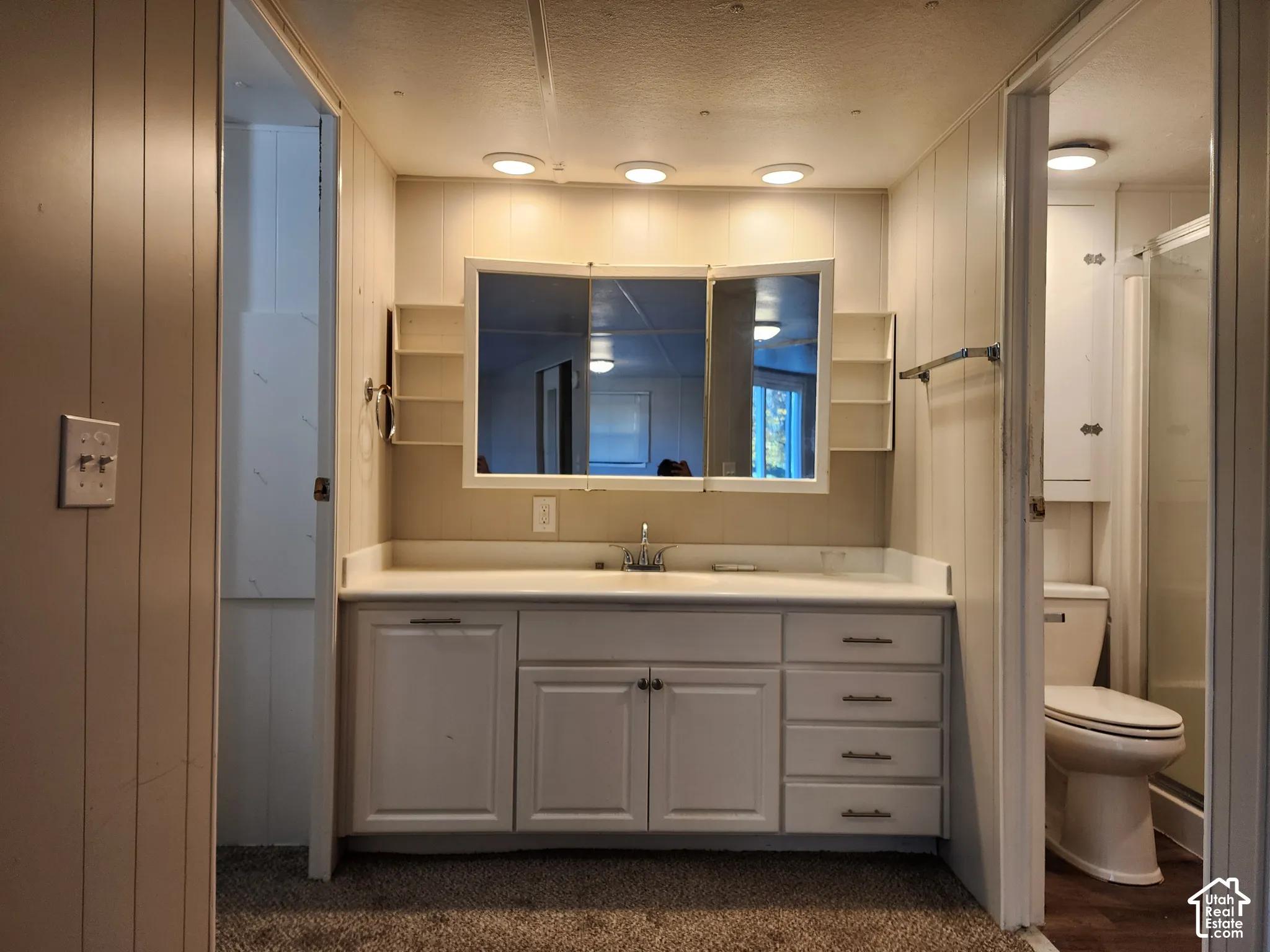 Bathroom vanity featuring white cabinetry, integrated countertop, tri-fold medicine cabinet with built-in side shelving, and recessed lighting