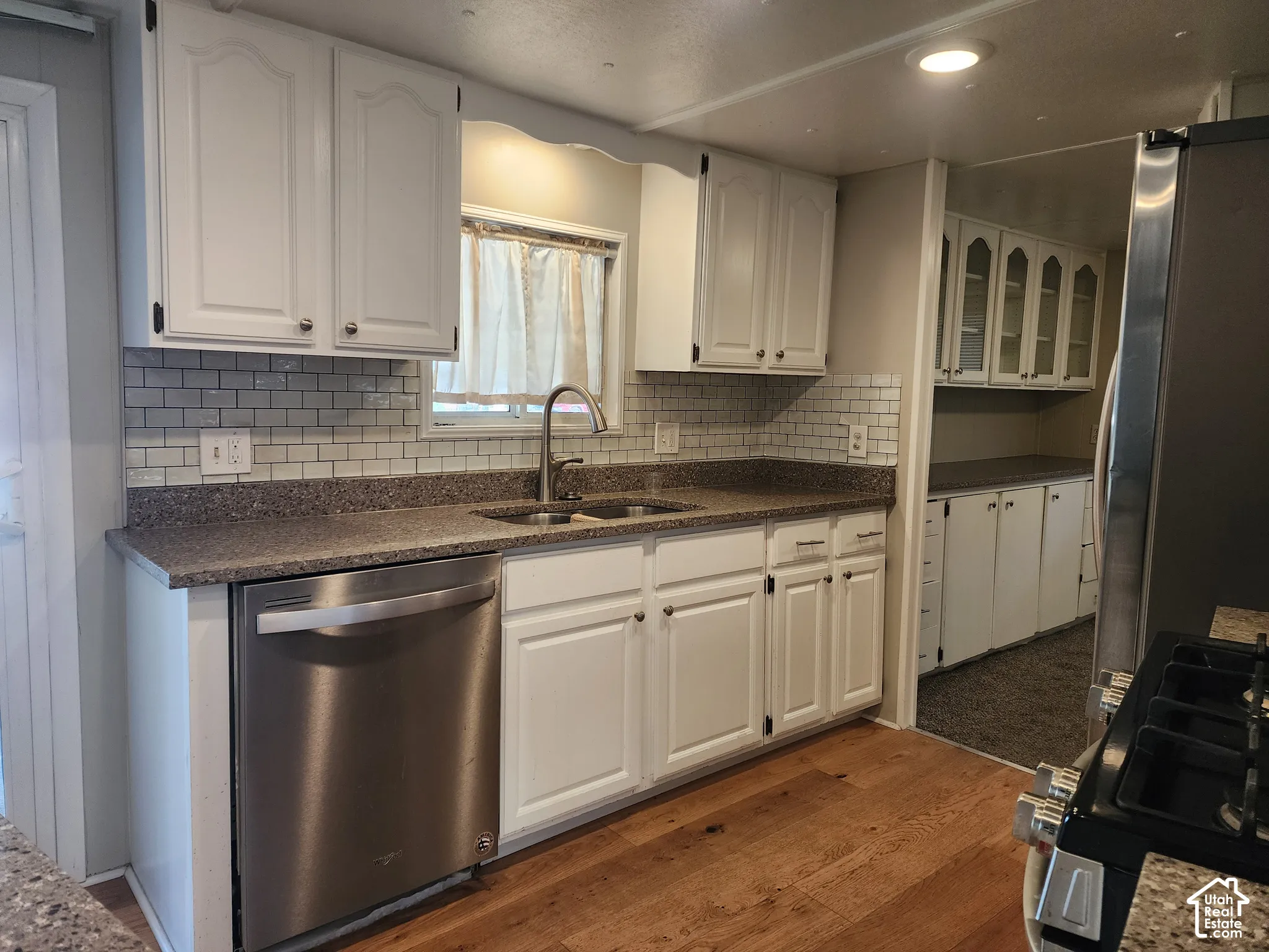Kitchen featuring white cabinetry, subway tile backsplash, stone-finish countertops, stainless steel dishwasher, and wood-finish flooring