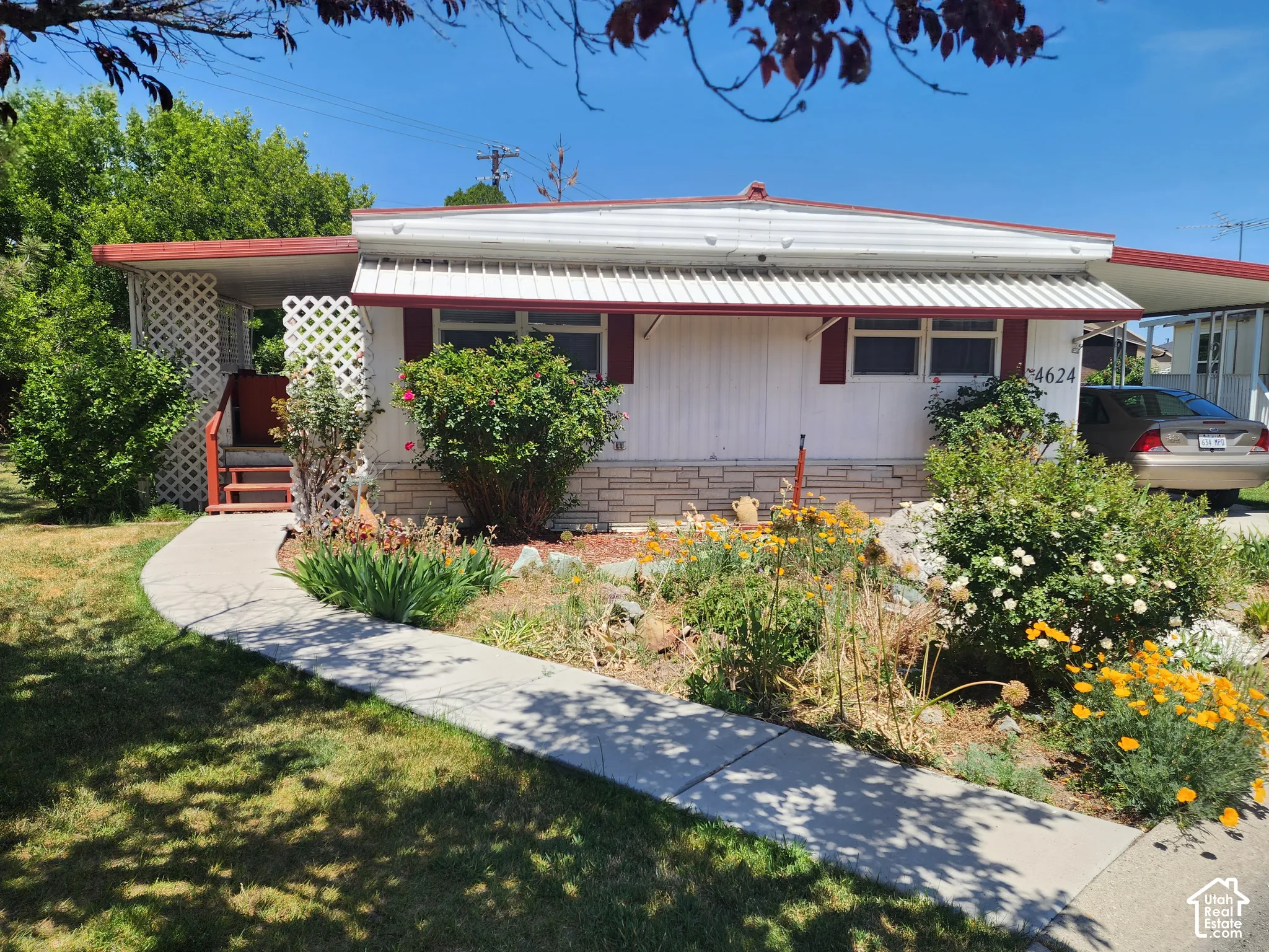 Exterior featuring stone veneer skirting, white horizontal siding, a metal awning, and a paved walkway leading to the entry