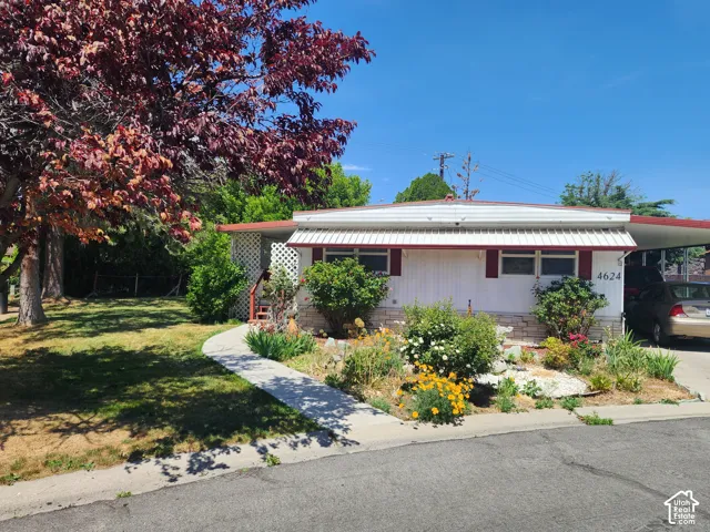 Single-level residence featuring a metal awning, stone-veneer skirting, a concrete walkway, and an attached carport