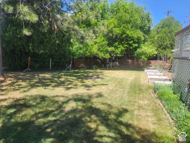Backyard featuring a grass lawn, perimeter lattice fencing, mature trees, and raised garden beds