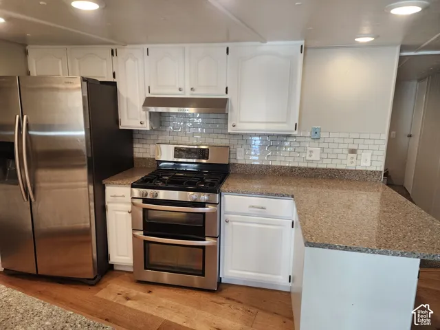 Kitchen featuring white cabinetry, stone-finish countertops, subway tile backsplash, stainless steel gas range with double ovens, and wood-finish flooring