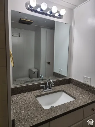 Full-width vanity featuring an integrated countertop with a drop-in sink, polished chrome faucet, expansive wall-mounted mirror, and a four-bulb vanity light fixture