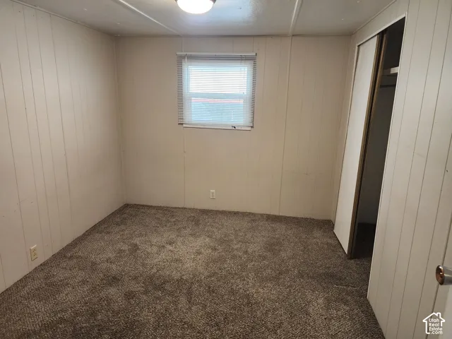 Neutral-toned wall paneling, wall-to-wall carpeting, single-pane window with mini-blinds, and sliding-door closet