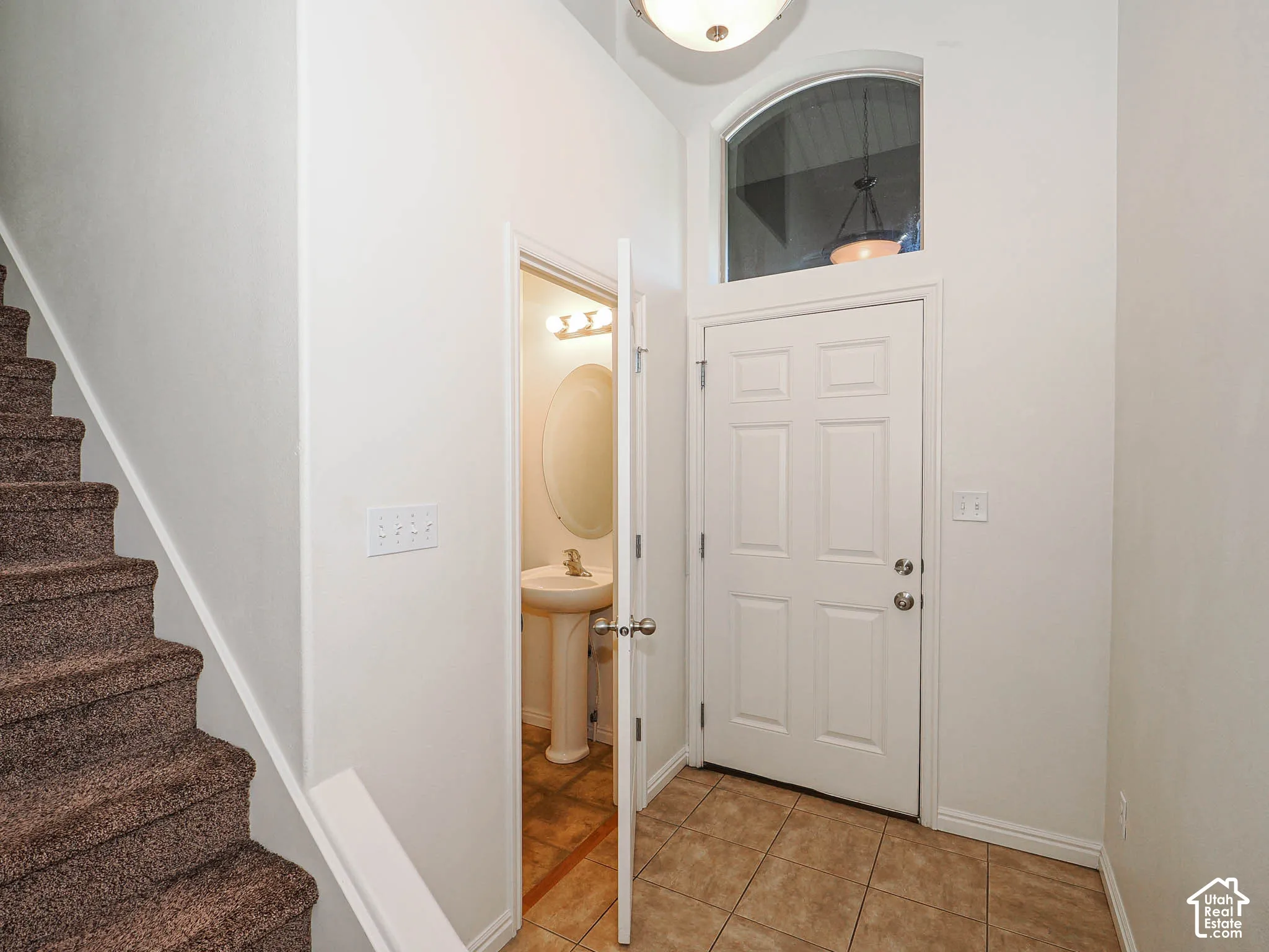 Entryway featuring high ceilings, a six-panel door with an arched transom window, ceramic tile flooring, and a pedestal sink in a separate area