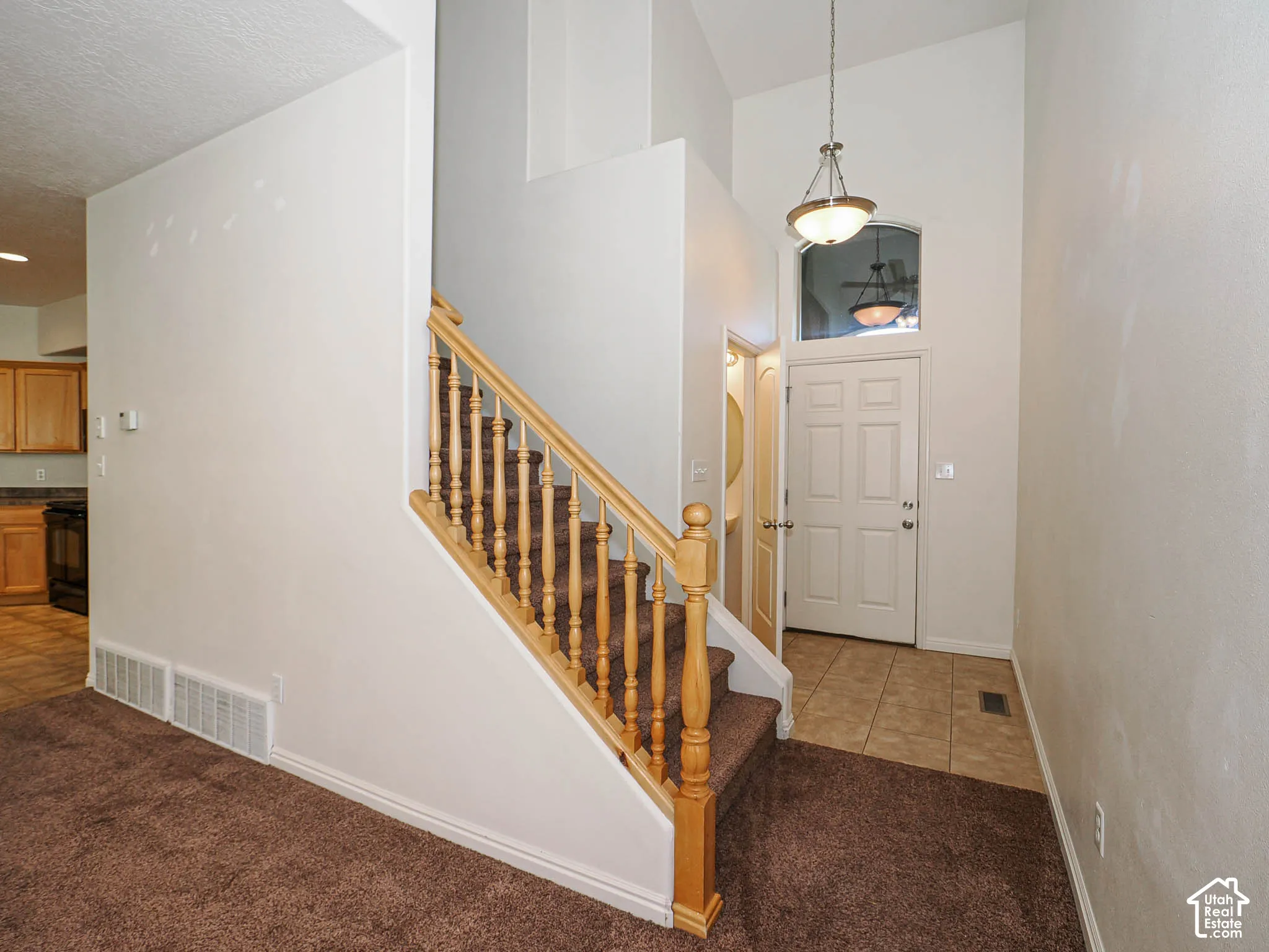 Entryway featuring vaulted ceilings, a suspended pendant light fixture, a wood-finish staircase railing, and ceramic tile flooring