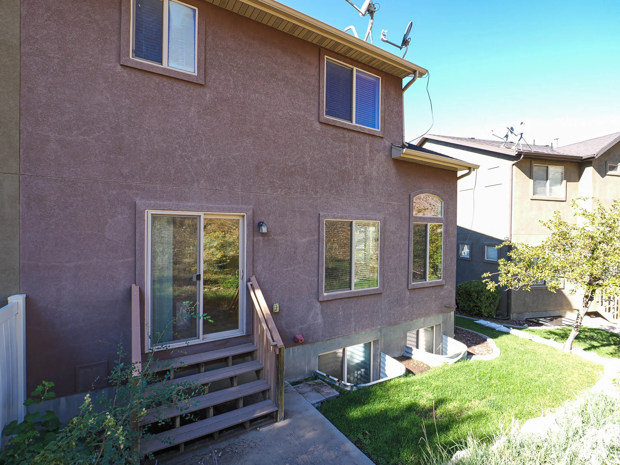 Stucco exterior featuring dual-pane windows, arched transom window, glass sliding door, and integrated window wells
