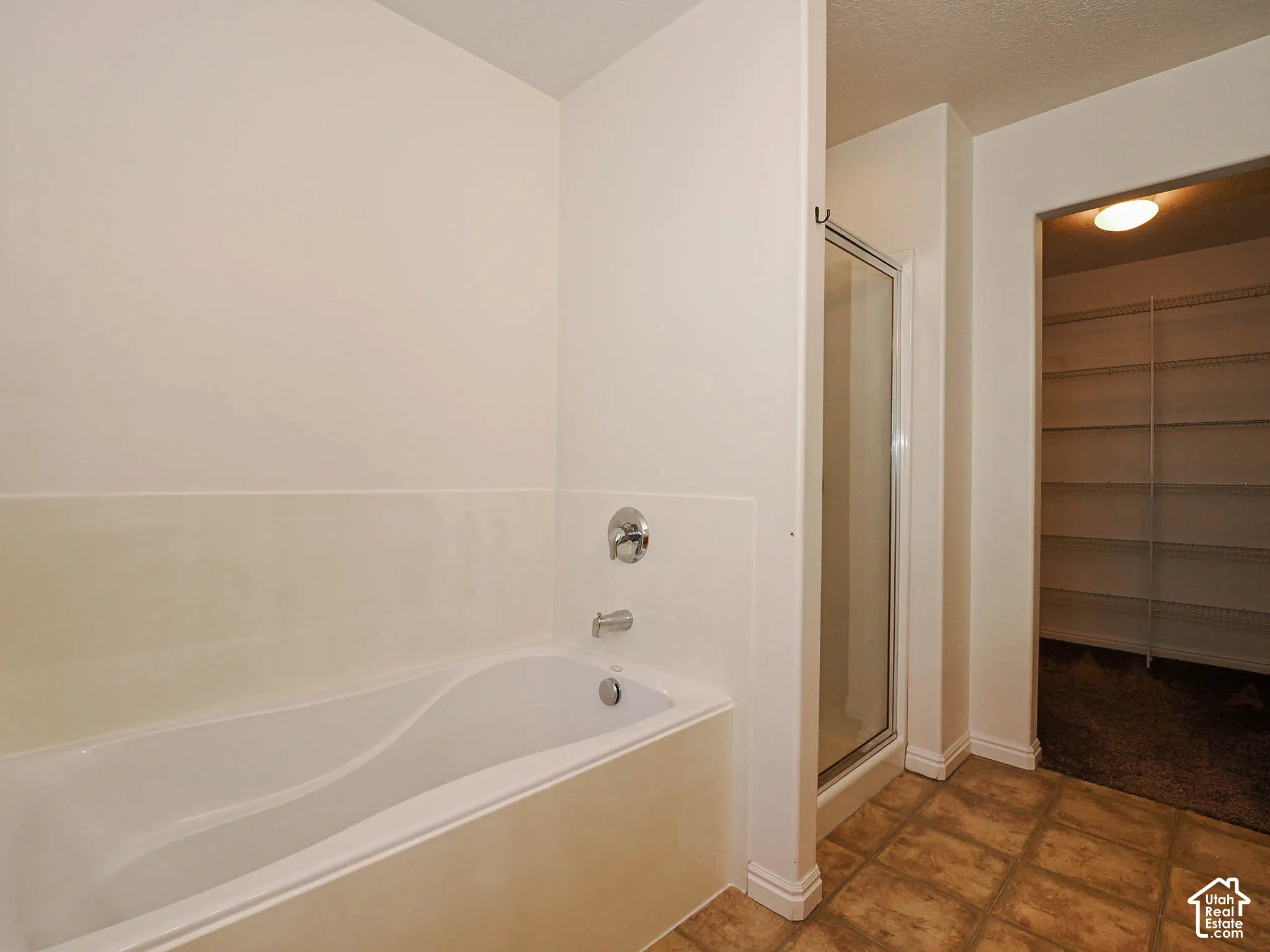 Soaking tub with wall-mounted chrome fixtures, glass-enclosed shower, tile flooring, and walk-in closet with built-in shelving