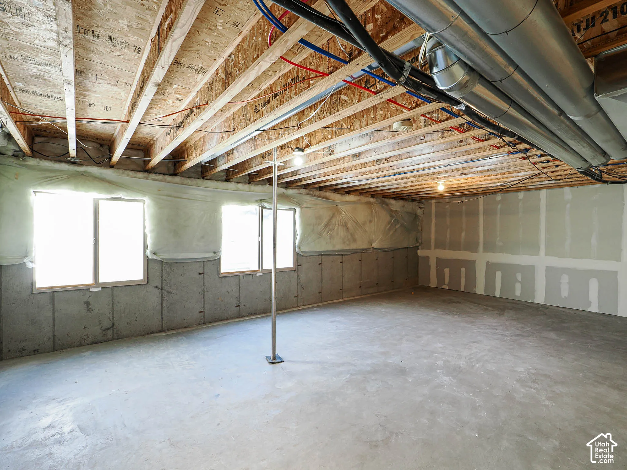 Unfinished interior space featuring exposed wood joists, concrete flooring, concrete foundation walls, and two windows