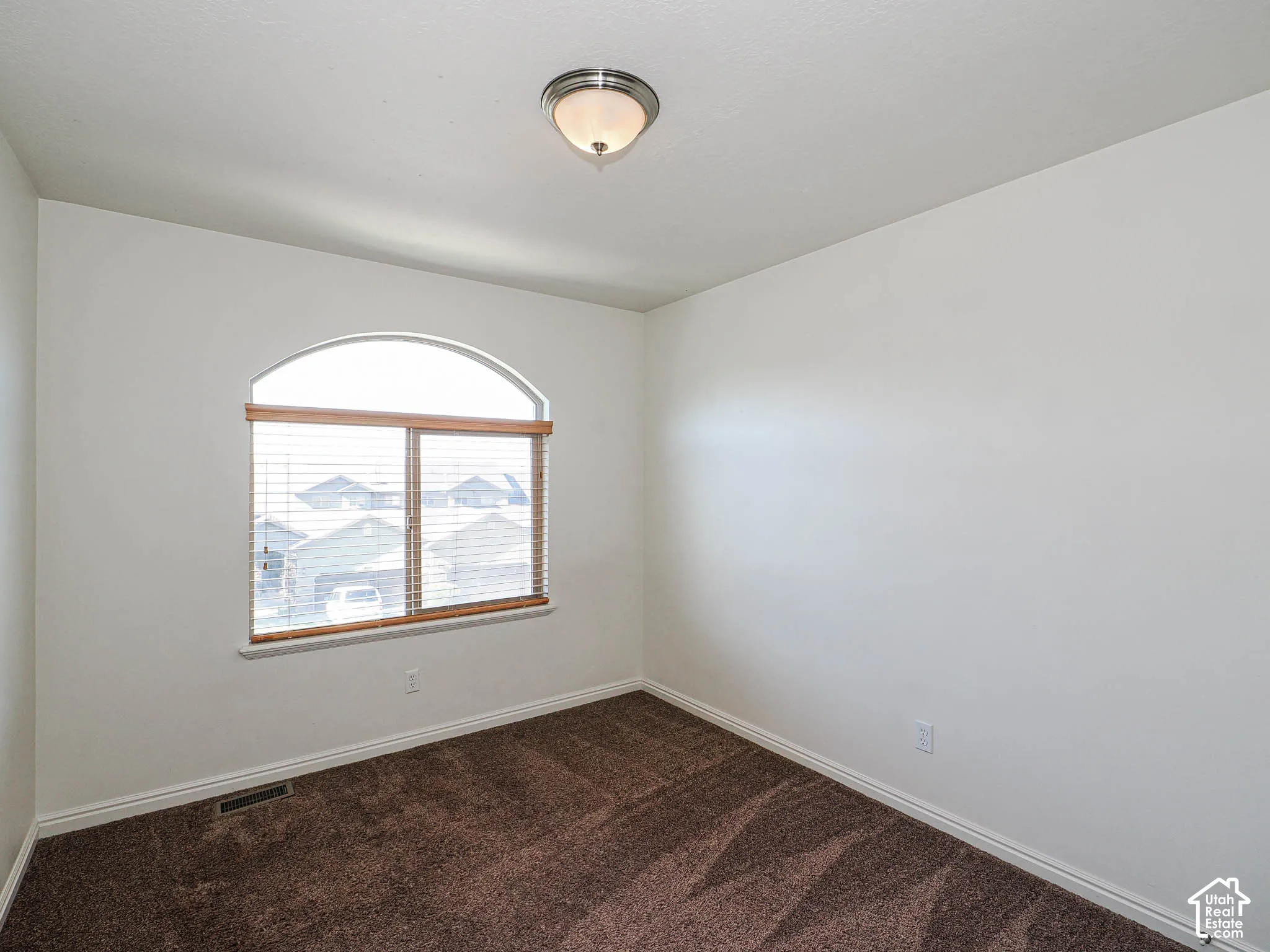 Room featuring neutral wall tones, arched window, and carpeted flooring with a flush-mount ceiling light fixture