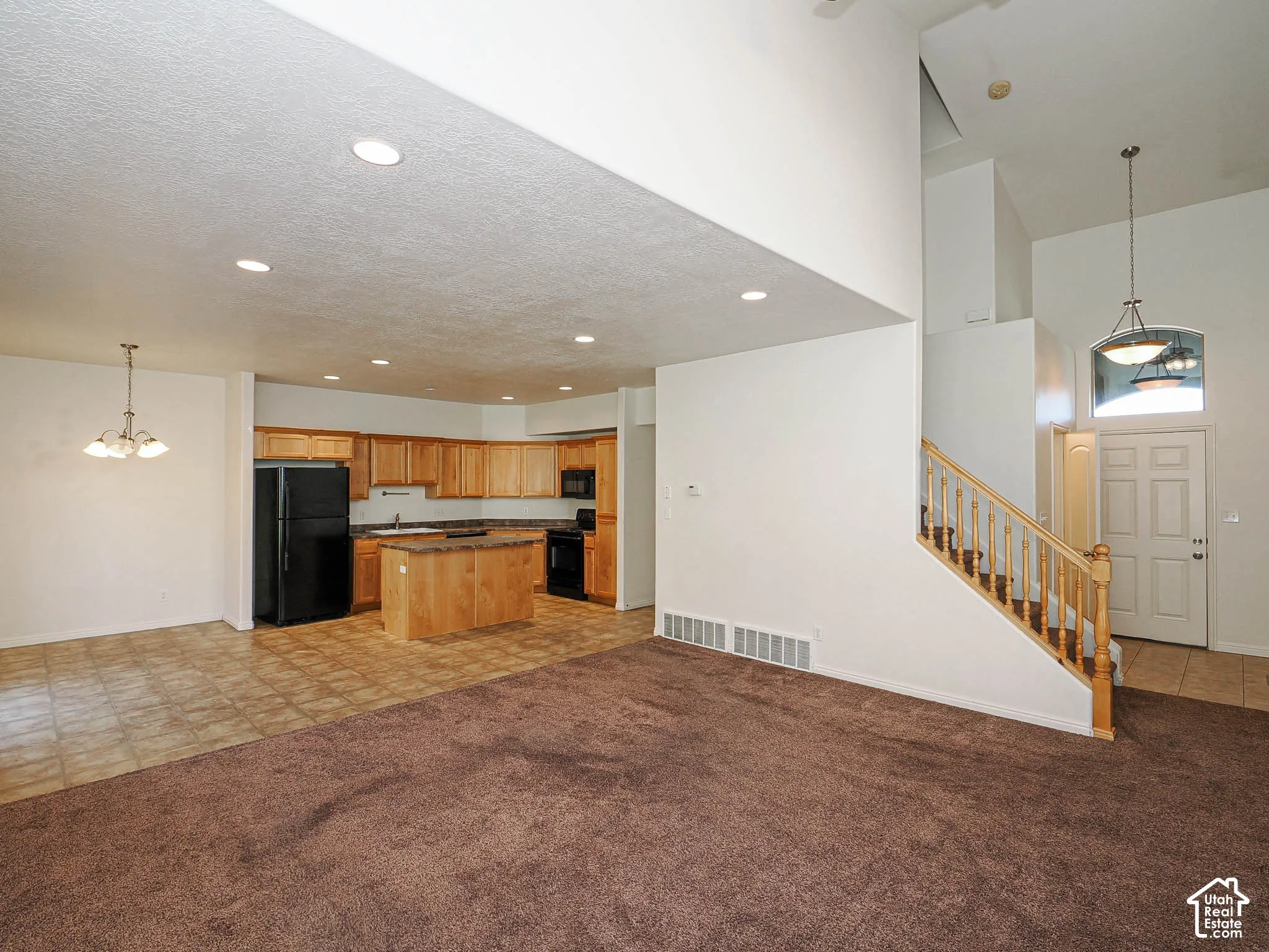 Open-concept interior featuring vaulted ceilings, recessed lighting, kitchen island, wood-finish cabinetry, and a staircase with a wooden railing