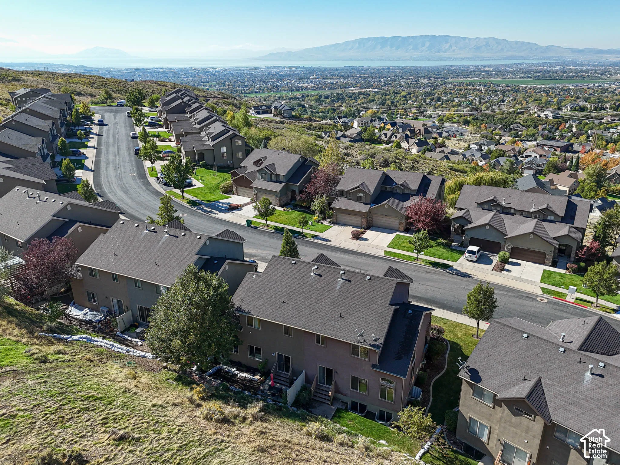 Elevated hillside residential community featuring multi-level dwellings with asphalt shingle roofing, paved roadways, and prominent mountain and valley scenery