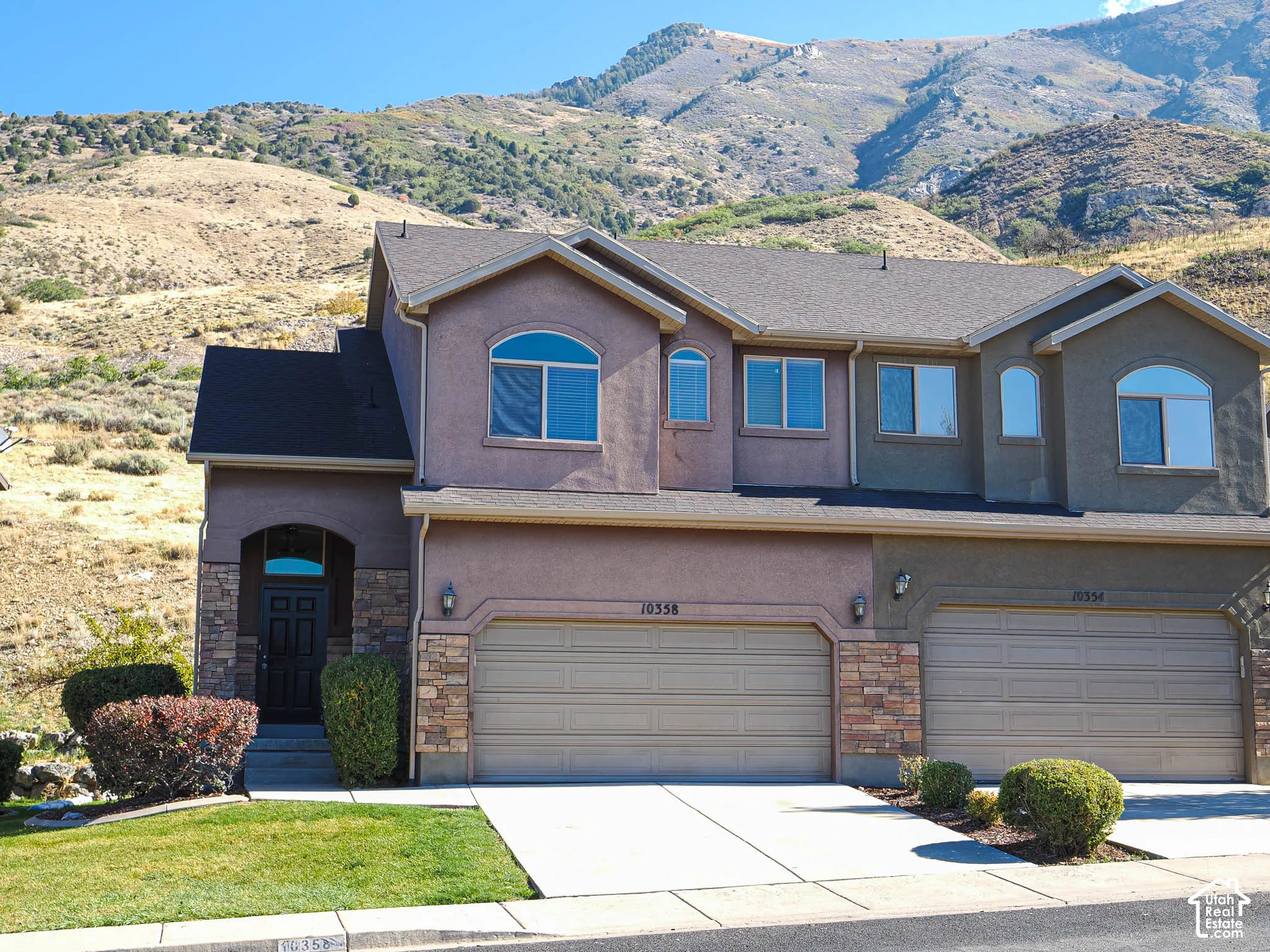 Two-story residence featuring multi-tone stucco exterior, stone veneer accents, arched windows, and two attached garages, set against a prominent mountain backdrop