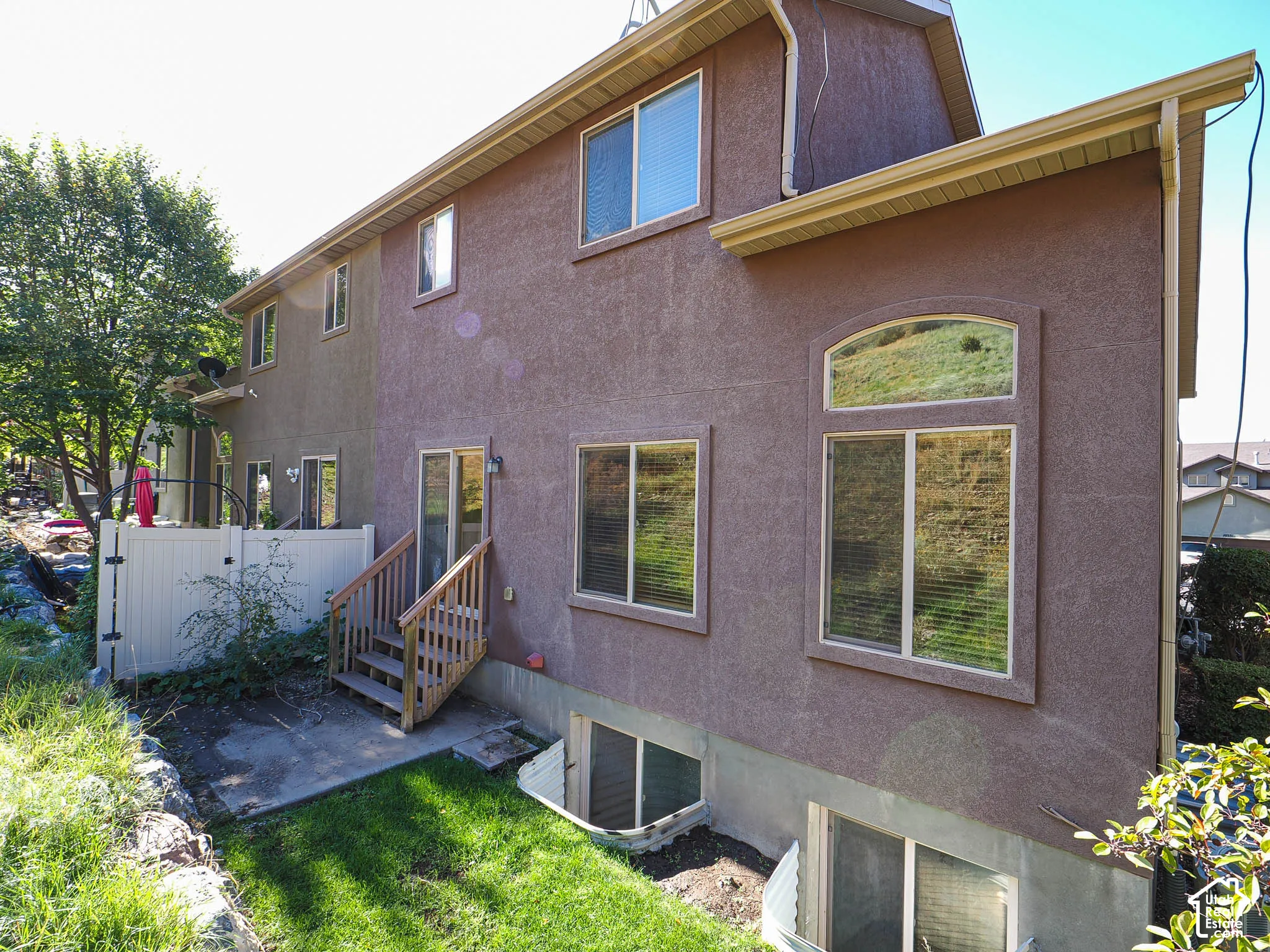 Stucco exterior featuring an arched window, a wood staircase, two egress window wells, and a white privacy fence