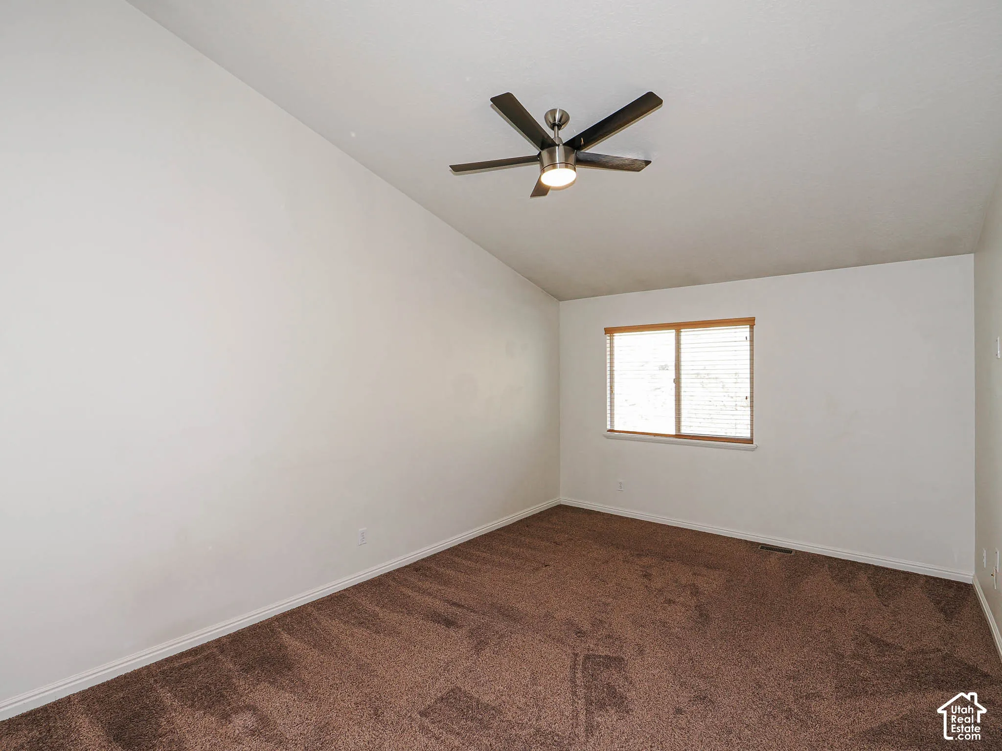 Vaulted ceiling featuring a central brushed-nickel finish ceiling fan with integrated lighting and wall-to-wall carpeting