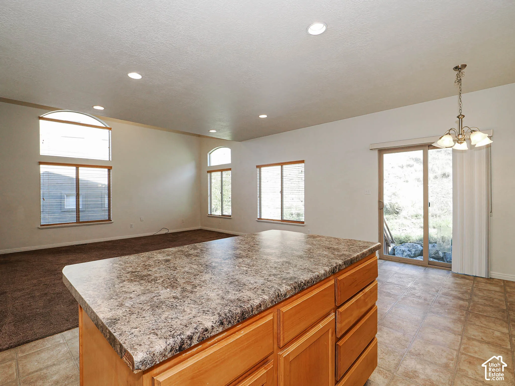 Kitchen island with laminate countertop, natural wood-finish cabinetry, recessed ceiling lighting, arched windows, and a sliding glass door