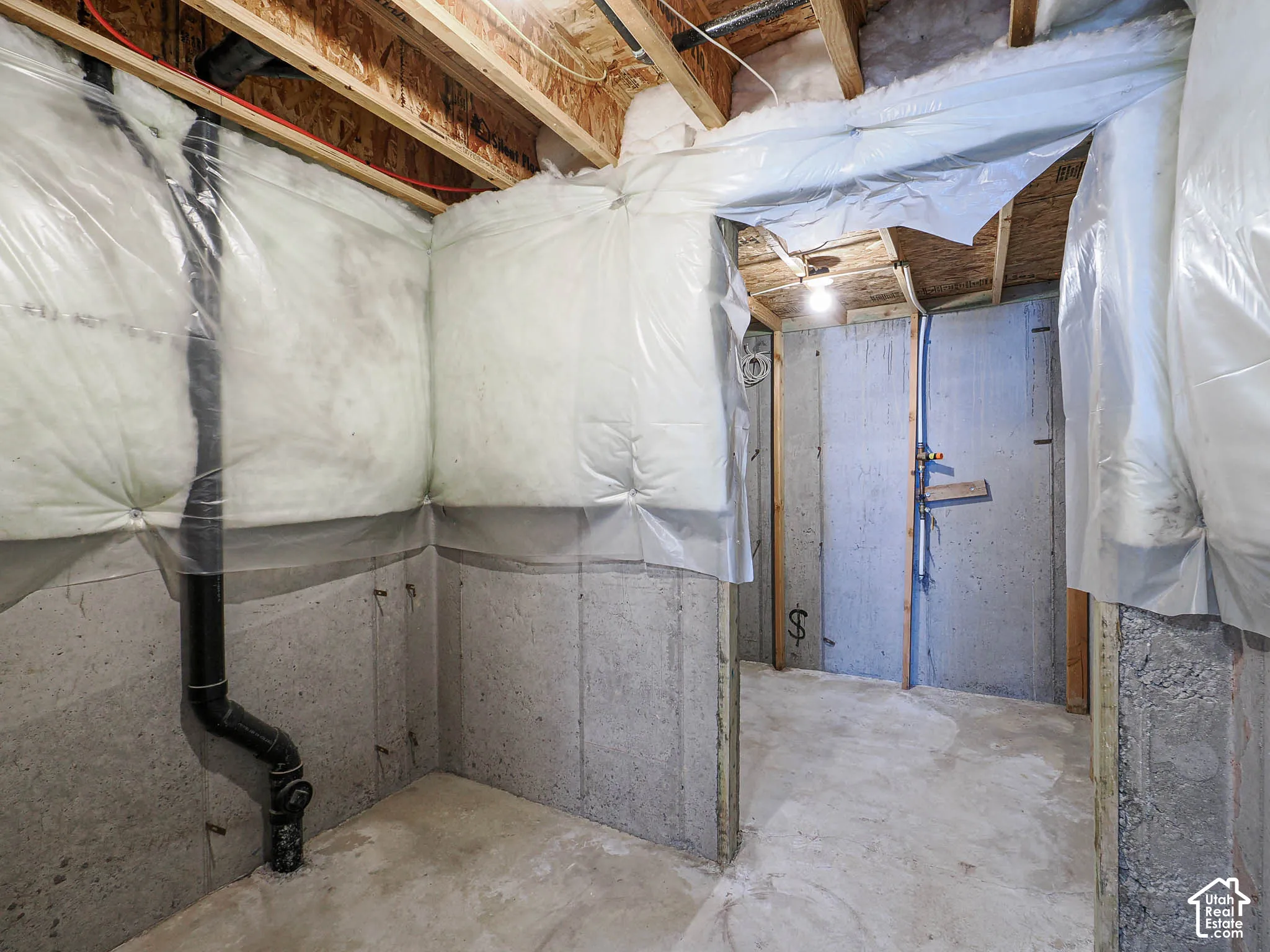 Unfinished utility area featuring exposed wood ceiling joists, concrete foundation walls, and vapor-barrier insulation