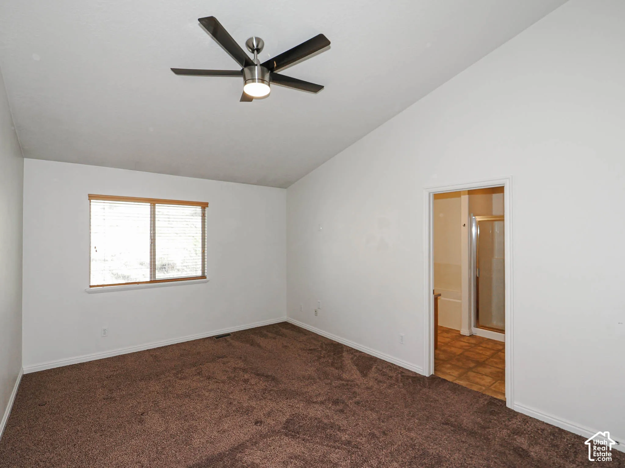 Vaulted ceiling, wall-to-wall carpeting, brushed metal ceiling fan with integrated light, and a double-pane window with horizontal blinds