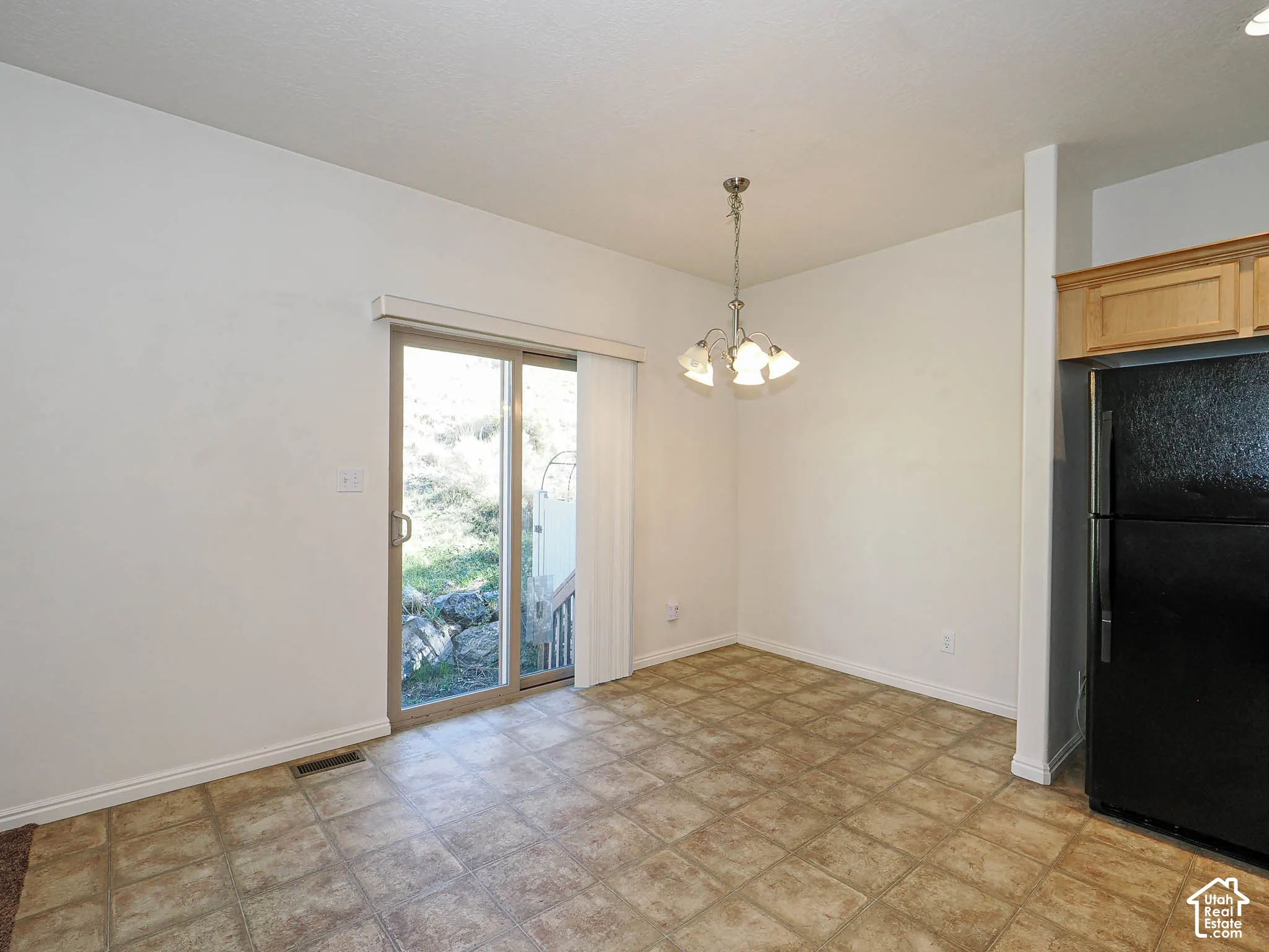 Tile flooring, glass sliding door, decorative multi-light chandelier, and natural wood-tone cabinetry