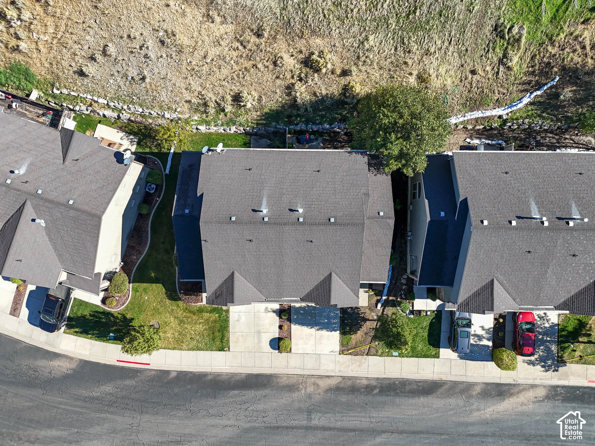 Aerial view of the residence featuring a multi-pitched shingled roof, concrete driveway, and landscaped yard space