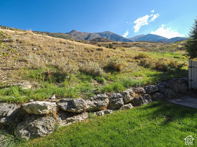 Expansive tiered lot featuring a natural rock retaining wall, landscaped grass area, and mountain scenery