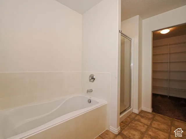 Soaking tub with wall-mounted chrome fixtures, glass-enclosed shower, tile flooring, and walk-in closet with built-in shelving