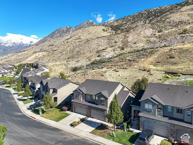 Aerial perspective of residential structures featuring multi-story gabled rooflines, stone and stucco facades, and attached multi-car garages, situated against a backdrop of mountain terrain