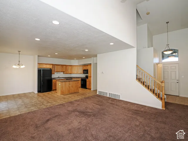 Open-concept interior featuring vaulted ceilings, recessed lighting, kitchen island, wood-finish cabinetry, and a staircase with a wooden railing