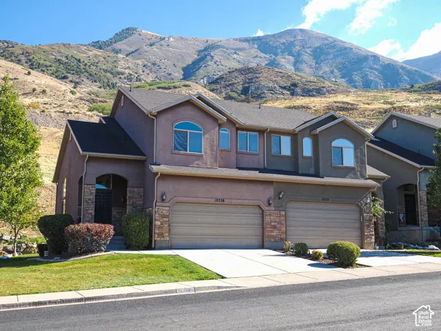 Multi-level exterior featuring stone veneer accents, stucco siding, arched window detailing, two-car garages, and a mountainous backdrop
