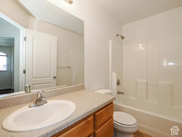 Bathroom featuring a wood-finish vanity with a stone-composite countertop, integrated sink, wall-spanning mirror, and a tub-shower combination with a surround