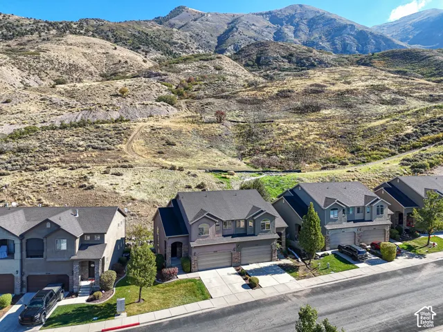 Multi-level residential structures featuring asphalt shingle roofing, multi-car garages, and concrete driveways, situated against a backdrop of mountainous terrain
