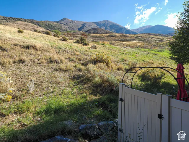 Expansive hillside landscape featuring natural terrain and a mountain backdrop, complemented by a white vinyl privacy fence and a metal garden arch