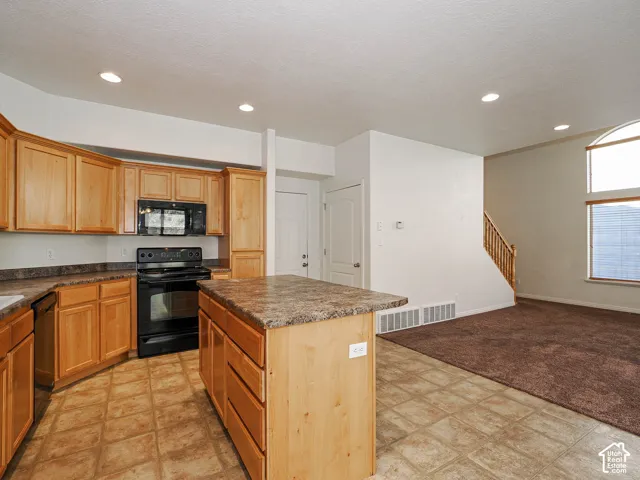 Kitchen featuring natural wood cabinetry, a central island with stone-finish countertop, integrated black appliances, tile flooring, and recessed lighting