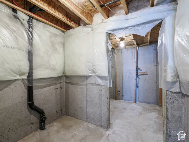 Unfinished utility area featuring exposed wood ceiling joists, concrete foundation walls, and vapor-barrier insulation