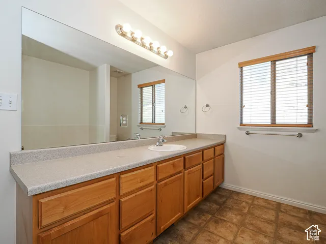 Bathroom vanity featuring natural wood-finish cabinetry, a large wall-mounted mirror, a neutral-toned countertop with an integrated basin, and a five-light fixture
