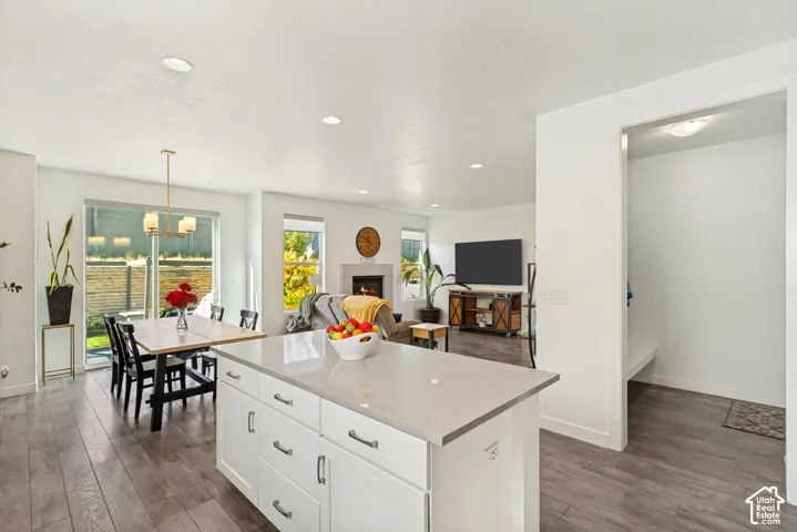 Kitchen featuring a center island with a solid surface countertop, white cabinetry, wood-finish flooring, recessed lighting, and a fireplace with a stone-finish surround