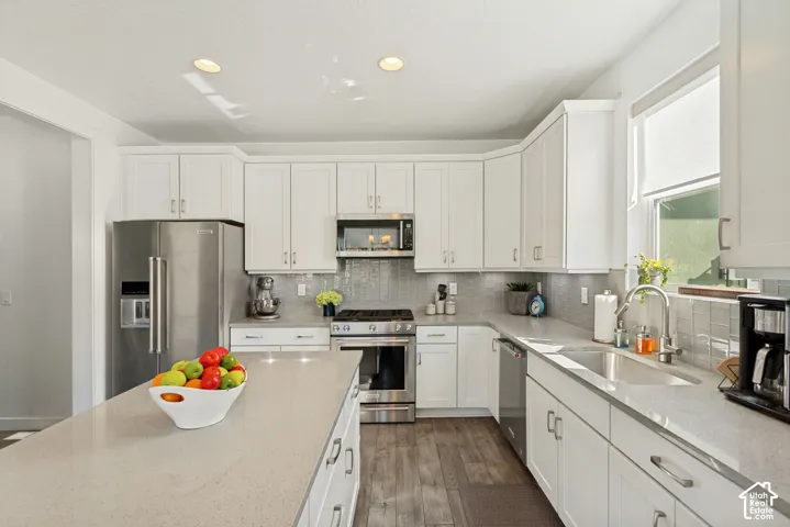 Kitchen featuring white shaker-style cabinetry, a quartz countertop island, stainless steel appliances, a tile backsplash, and wood-finish flooring