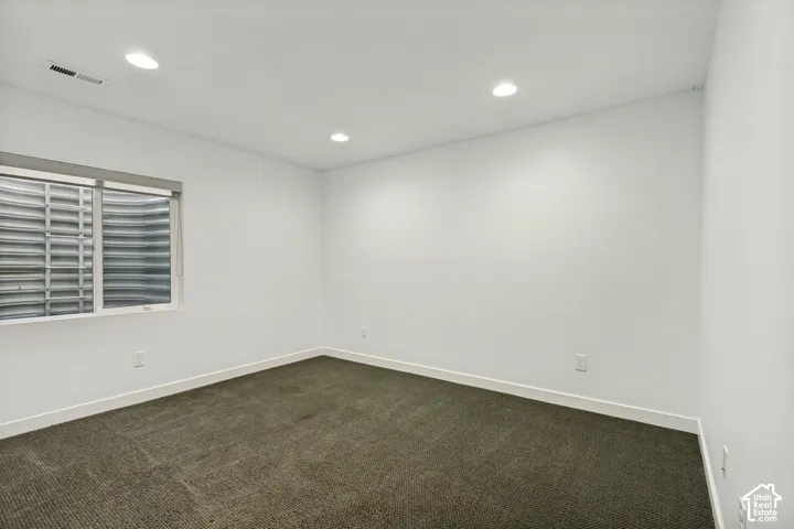 Neutral-toned carpeted flooring, recessed lighting, and a corrugated metal window well