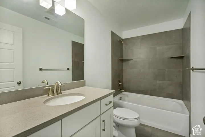 Bathroom featuring a light-toned vanity with a solid-surface countertop, an undermount sink, large-format tile tub surround, and polished metal fixtures