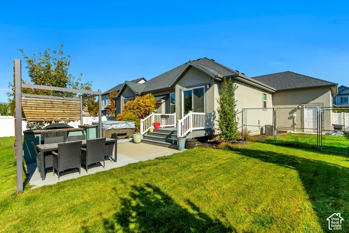 Rear exterior featuring a concrete patio, elevated deck with white railing, wood-slat pergola, and chain-link fenced yard