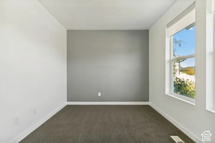 Interior space featuring a neutral color palette, grey accent wall, wall-to-wall carpeting, and a window with a roller shade