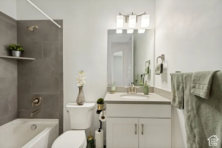 Bathroom featuring a vanity with a neutral-tone countertop, an integrated sink, a rectangular mirror, a three-light fixture, and a tub-shower combination with full-height tile surround